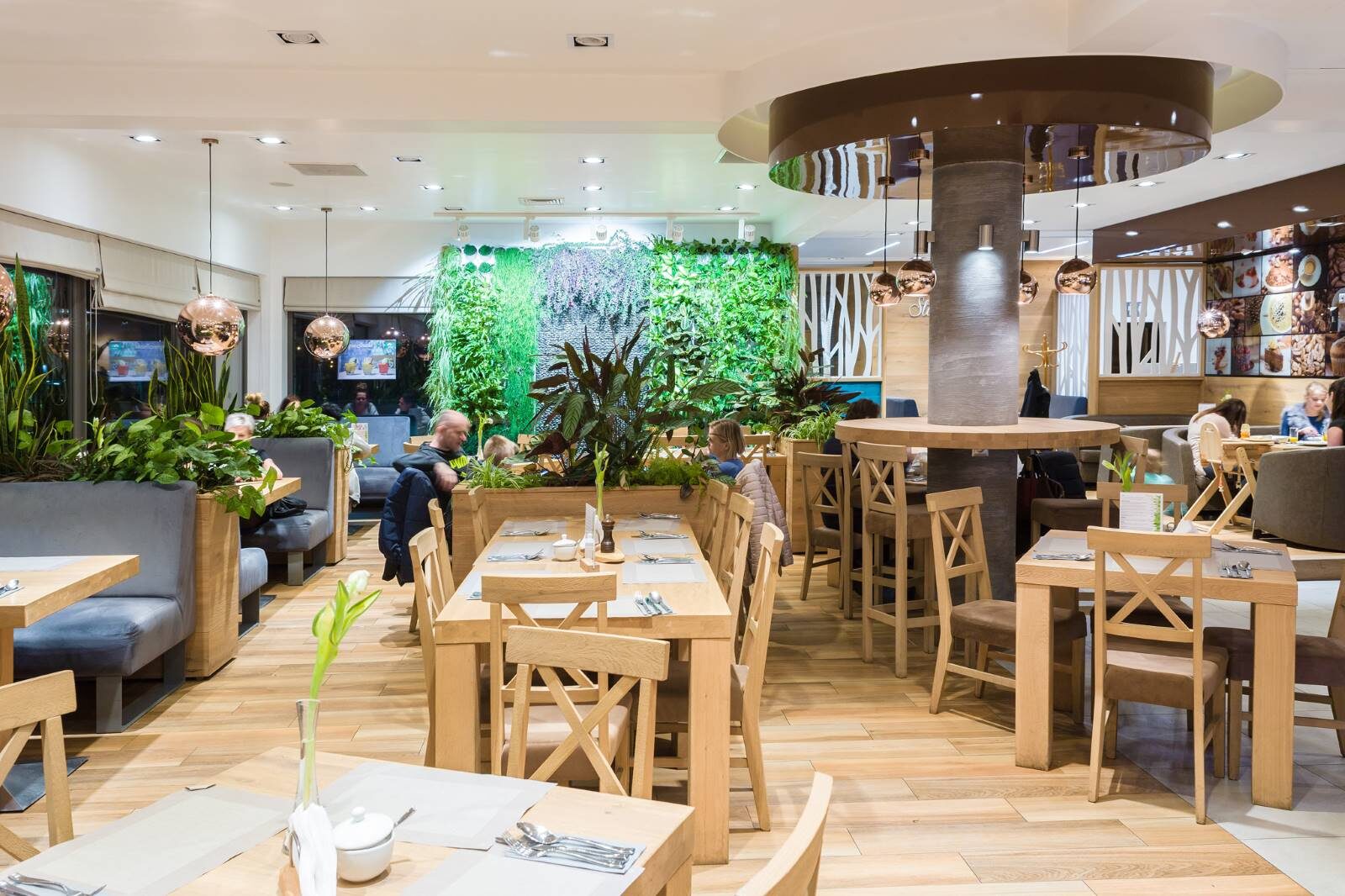 Sala restauracji Stacja Smaku — drewniane stoły i zielona ściana z roślin